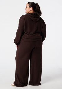 Bruine geribde hoodie met een capuchon, gecombineerd met loszittende bruine broek. De stof heeft een zachte textuur, ontworpen voor comfort en bewegingsvrijheid.