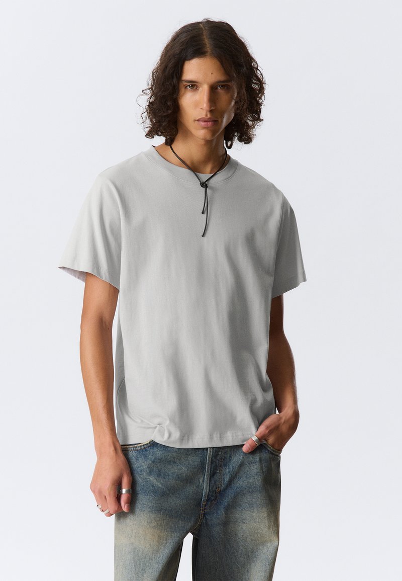 Tricou din bumbac gri cu mâneci scurte, croială relaxată, decolteu rotund și detaliu răsucit la tiv. Purtați-l cu blugi albaștri decolorati.