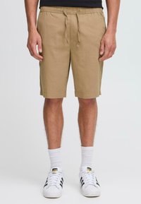 Beige shorts laget av mykt stoff, med elastisk midje og snor, sidelommer og en avslappet passform, som når midt på låret.