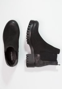 Botines negros con suelas gruesas y estriadas, paneles laterales elásticos y detalle texturizado en el tacón, mostrados desde vistas superior y lateral sobre un fondo blanco.