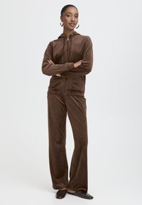 Ensemble de survêtement en velours marron avec une capuche zippée et un pantalon droit, présentant une texture douce et un design minimaliste.