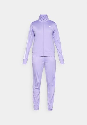 Lilla treningsdrakt med en glidelåsjakke med høy krage og hvite sidestreker, sammen med matchende bukser. Jevn tekstur av stoffet.