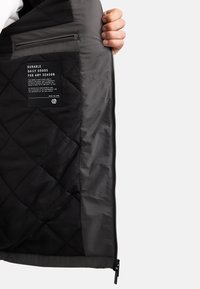 Intérieur de veste matelassée noire avec une doublure lisse, dotée d'une poche zippée et d'une étiquette textile avec des instructions d'entretien.