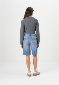 Grå langermet topp, lyseblå denimshorts med rullet kant og beige joggesko med rosa detaljer, sett bakfra.