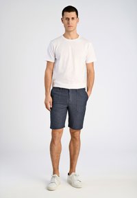Herrarnas avslappnade outfit med en enfärgad vit t-shirt och mörkblå shorts med ett subtilt mönster. Vita sneakers fulländar looken.