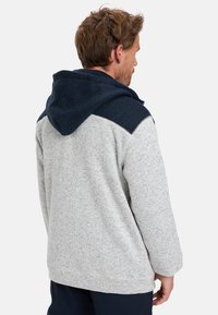 Sudadera de forro polar en gris claro con capucha azul marino. Presenta un acabado texturizado, diseño oversize y acentos en los hombros de color contrastante.