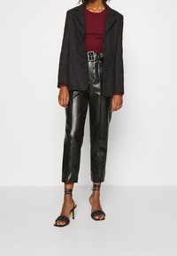 Black fitted blazer, ribbed burgundy top, and high-waisted black leather pants with a belt. High-heeled black sandals complete the outfit.