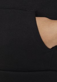 Black sweatshirt fabric close-up showcasing a hand in a side pocket. Smooth texture with visible stitching and soft material.