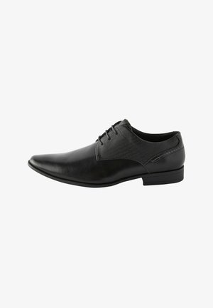 Scarpa da uomo in pelle nera con punta affusolata, pannello in tessuto laterale e lacci sottili. Presenta una texture liscia e un tacco basso.