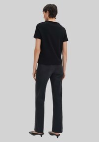 Zwarte top met korte mouwen en een ronde hals, gecombineerd met donkere, recht gesneden denim jeans en zwarte puntige schoenen.