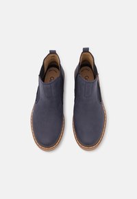 Scarpe slip-on blu navy con pannelli elastici laterali, tomaia in pelle liscia, punta rotonda e cuciture in un marrone chiaro a contrasto attorno alla suola.
