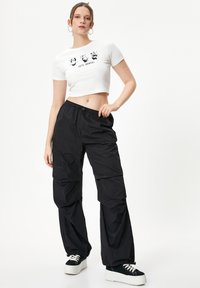 Camiseta blanca cropped con gráficos de panda y el texto "¡Bailamos!", combinada con pantalones negros de corte suelto y zapatillas de plataforma negras.