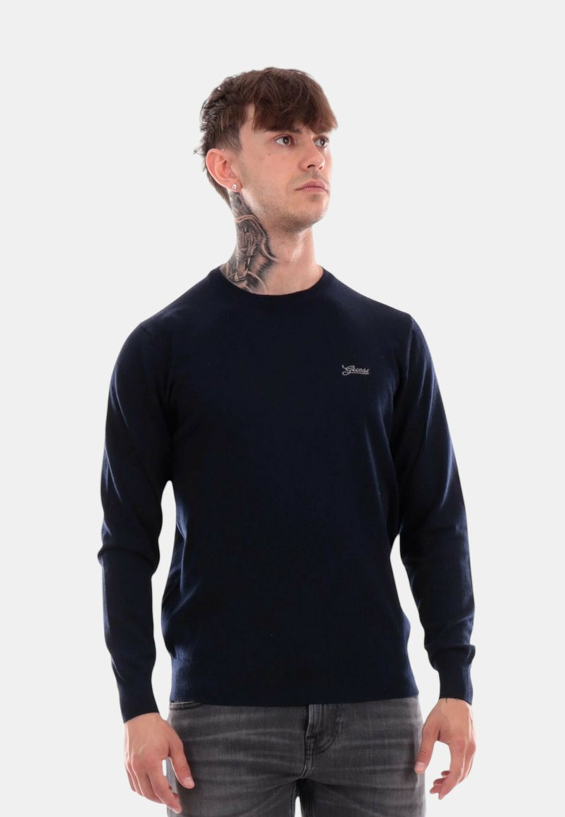 Maglione blu navy a maniche lunghe con scollatura rotonda e polsini a coste, caratterizzato da un piccolo logo ricamato sul petto. Texture liscia.