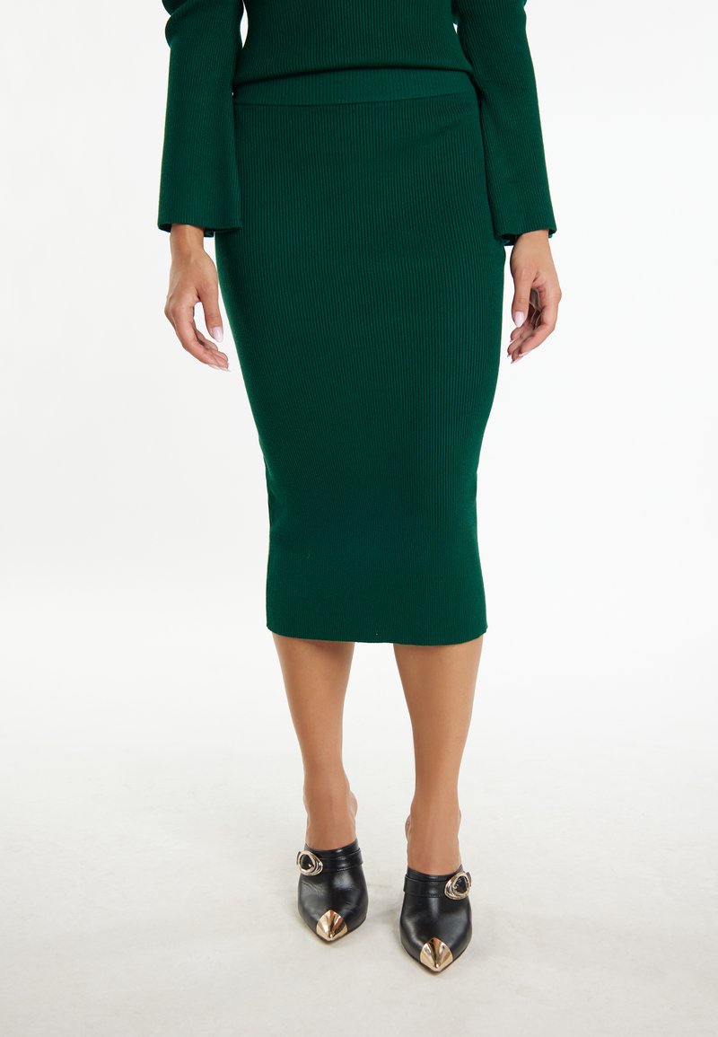 Groene geribbelde midi-rok, getailleerde vorm, textuurstof. Zwarte hakken met een spitse neus en gouden hardwareaccenten. Eenvoudig, elegant ontwerp.