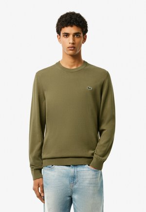 Olive green long-sleeve sweatshirt with round neckline, ribbed cuffs and hem, featuring a small embroidered crocodile logo on the chest.