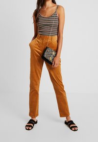 Randig linne, orange kordflöjlbyxor, svart crossbody-väska med geometriskt mönster och svarta sandaler med remmar och låg klack.