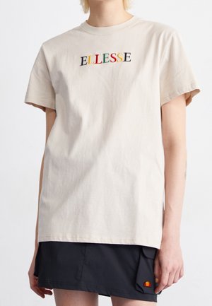 Beige Baumwoll-T-Shirt mit kurzen Ärmeln, mit gesticktem "ELLESSE"-Logo in mehreren Farben. Getragen mit einem schwarzen Rock, der Logodetails zeigt.