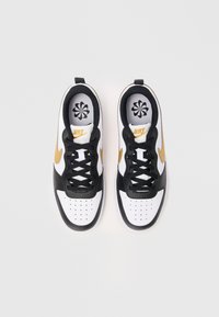 Une paire de baskets Nike blanches, noires et dorées vue d'au dessus, avec des lacets noirs et le logo Nike sur les semelles intérieures et sur les côtés.