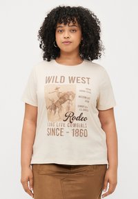 Beige kokvilnas t-krekls ar vintage rodeo grafiku, kas izceļ Rietumu motīvus, brūnu tekstu un brīvu piegriezumu. Apaļa kakla izgriezums un īsas piedurknes.