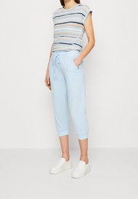 Lichtblauwe cropped broeken met elastische boorden en een taille met trekkoord, gecombineerd met een gestreepte T-shirt met korte mouwen in pastelkleuren. Witte instappers.