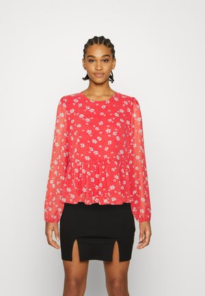 Blusa longa de mangas vermelha com flores, com uma cintura peplum, textura transparente e decote redondo, acompanhada de uma saia mini preta com detalhes de fenda.