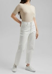 Maglione beige a maniche corte con dettaglio a palloncino abbinato a jeans bianchi a vita alta e sneakers bianche. Design semplice, vestibilità casual.