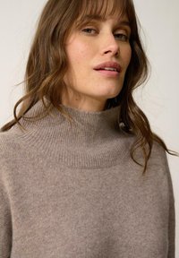 Beżowy sweter z golfem wykonany z miękkiej, teksturowanej dzianiny, z wysokim kołnierzem i ribbami przy dekolcie.