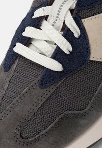 Herrskor med övre i grå mesh och mocka, vita snören, marinblå detaljer, texturerad yta och en beige panel längs sidan.