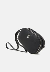 Borsa a tracolla in pelle nera con texture, zip argentata e piccolo logo metallico sul fronte, esposta su sfondo bianco.