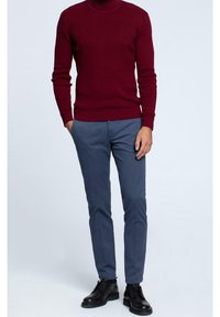 Maglione a collo alto ribbed bordeaux con maniche lunghe, abbinato a pantaloni blu navy slim-fit e scarpe nere stringate. Design e texture minimalisti.