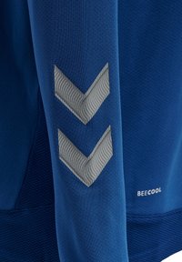 Blå atletisk skjorte med tekstureret stof, grå chevronmønstre på ærmet og "BECOOL" branding nær kanten.