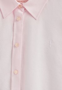 Ljusrosa bomullspolo med en strukturerad krage, fem knappar och en liten vit broderad figur på vänster sida. Regular fit-design.