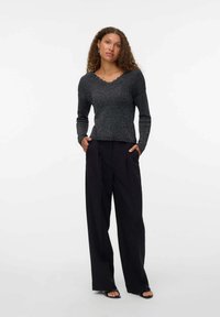 Top largo negro texturizado de manga larga con cuello festoneado, combinado con pantalones de pierna ancha negros de cintura alta y sandalias negras.