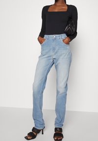 Ljusblå denimjeans med rak passform, hög midja och bälteshällor. Matchade med en svart långärmad topp och svarta klacksandaler.