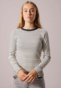 Pitkähihainen raidallinen paita, jossa on ribbitekstuuri, mustia raitoja valkoisella taustalla ja musta pyöreä pääntie.