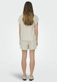 Beżowa lniana bluzka z krótkim rękawem zestawiona z pasującymi beżowymi szortami. Strój ma luźny krój oraz gładką teksturę. Obuwie w jasnym kolorze.