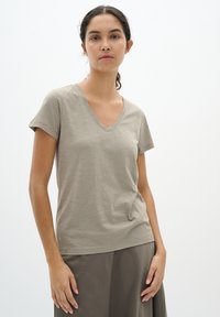 V-hals, kortdurende t-shirt in zachte, lichtgrijze stof, met een ontspannen pasvorm en subtiele textuur. Gecombineerd met een donkere rok.