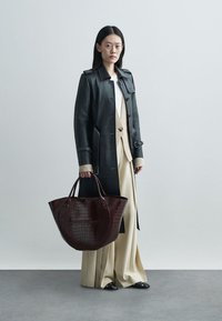 Μαύρο δερμάτινο παλτό με λεπτομέρειες από κουμπιά, μπεζ cardigan, ελεφαντόδοντο πλισέ παντελόνι και γυαλιστερή μπορντό τσάντα tote με σχέδιο κροταλία.