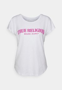 Bílá tričko s uvolněným střihem, krátkými rukávy a velkým růžovým potiskem s nápisem "TRUE RELIGION BRAND JEANS" na přední straně.