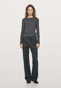 Dark gray long-sleeve top with a crew neckline paired with loose, dark denim jeans. Model wears black ankle boots. Minimalist aesthetic.