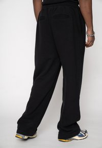 Pantaloni negri de trening cu croială lejeră, prevăzuți cu talie elastică și două buzunare în spate. Materialul pare moale, cu o textură fină.