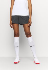 Nike sportovní šortky tmavě šedé barvy, doplněné bílými podkolenkami s černým logem a bílými kopačkami s červenými akcenty.