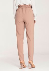 Spodnie z jasnoróżowego materiału z dopasowanym elastycznym paskiem w talii, zwężanym kroju i gładką fakturą, w połączeniu z przezroczystymi sandałami na obcasie.