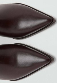 Braune Lederpumps mit spitz zulaufender Schuhspitze, glatter Oberfläche, detaillierter Naht entlang der Kanten und einem schlanken Design, das den oberen Bereich hervorhebt.