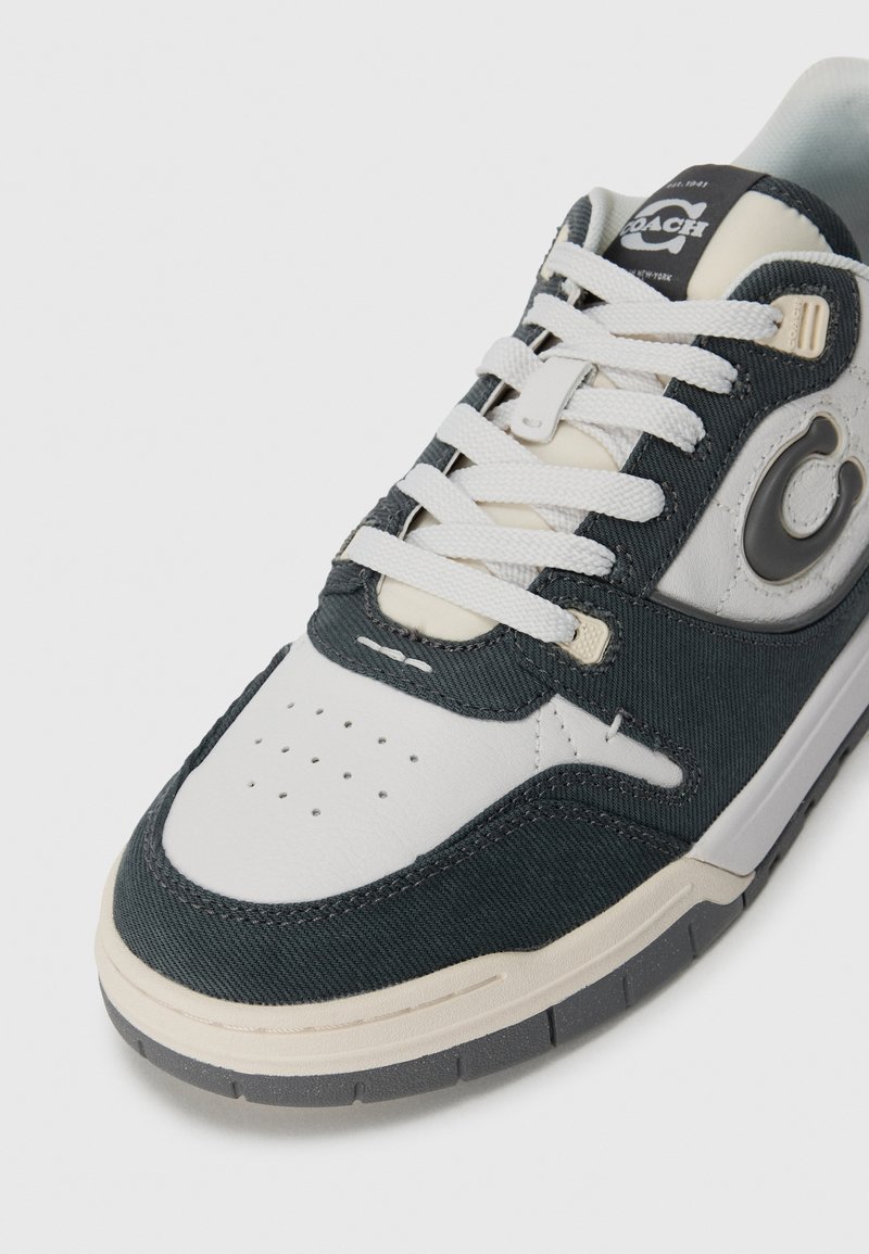 White and dark gray Coach sneaker with white laces, perforated toe, and branded logo on the side and tongue.