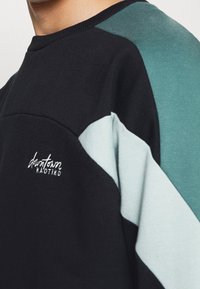Felpa nera in cotone con un design a blocchi di colore in teal e azzurro chiaro, con scollo rotondo e logo ricamato sul petto.