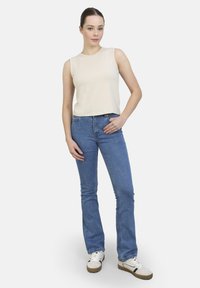 Top sin mangas beige con cuello redondo, combinado con jeans de campana azul claro y zapatillas blancas con detalles negros.