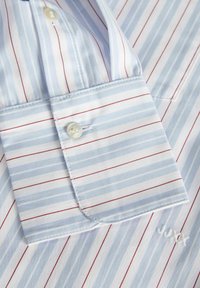 Modrá a bílá pruhovaná košile s červenými akcenty, se zapínáním na knoflík na manžetě a vyšitým logem, vyrobená z hladké tkaniny s ostrým povrchem.