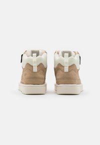 Zapatillas de ante marrón de media altura con acentos de malla blanca, cordones planos y una suela de goma beige, con una pestaña en el talón.