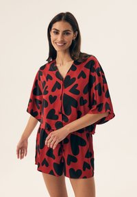 Red short-sleeve set featuring a V-neckline and black heart pattern, made from smooth fabric with a loose fit and drawstring waistband.